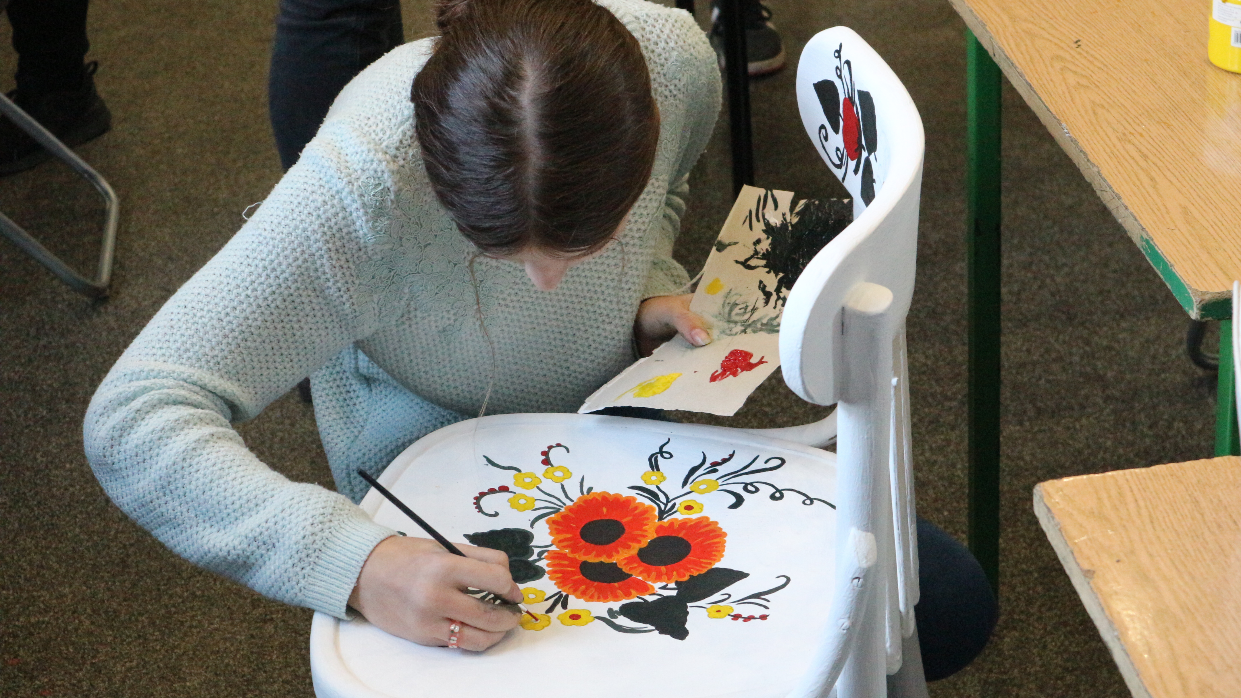 Uczennica z Ukrainy maluje na krześle wzory ludowe.