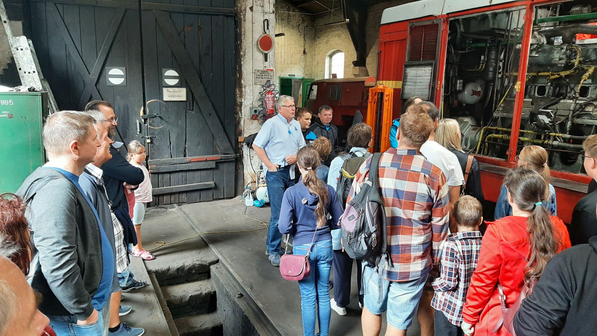 Turyści w hali napraw wraz z przewodnikiem Romanem Oberajem prezentującym silnik lokomotywy Lxd2
