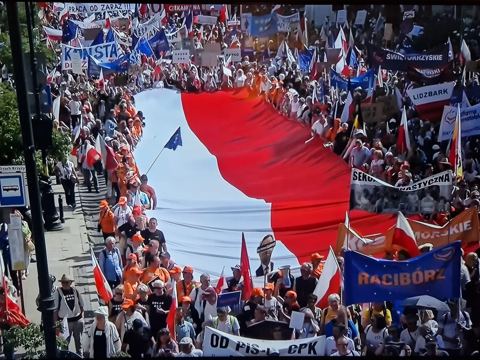 Screen z przekazu tv, gdzie raciborski transparent widać obok flagi narodowej